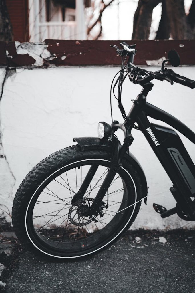 A detailed shot of an electric bicycle leaning against a white urban wall.